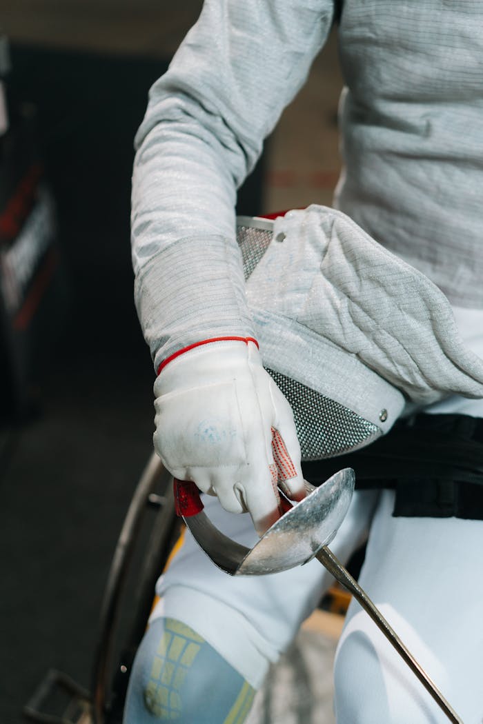 Focused view of a wheelchair fencer holding a sabre, preparing for a match.